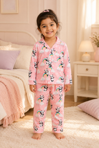 Child wearing pink pajamas with panda and rainbow patterns in a bedroom.