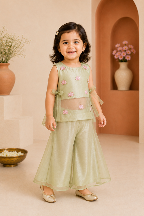 Young girl in a light green traditional outfit with pink floral patterns standing in a decorated room.
