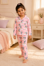 Child wearing pink pajamas with panda and rainbow patterns in a bedroom.