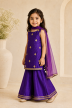 Young girl in a purple traditional outfit with gold accents standing against a neutral background.