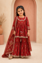 Young girl in a red traditional outfit standing in a softly lit room.