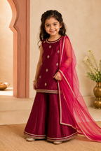 Young girl in a maroon traditional outfit with a maroon dupatta standing indoors.